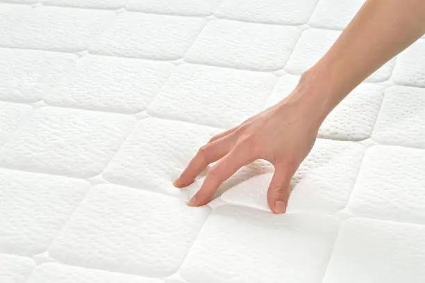 Choosing mattress and bed. Close-up of female hand touching and testing mattress in a store. Copy space.