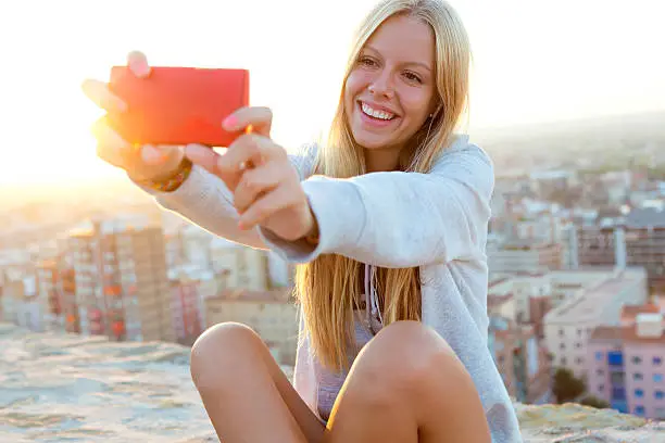 Outdoor portrait of beautiful blonde girl taking a selfie on the roof.