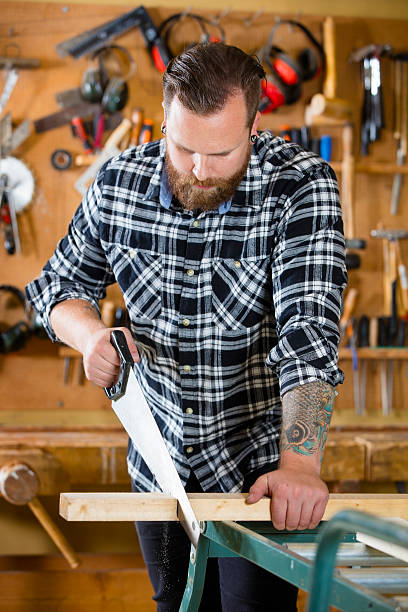 istock Carpenter sawing wood with hand saw in workshop 512434438