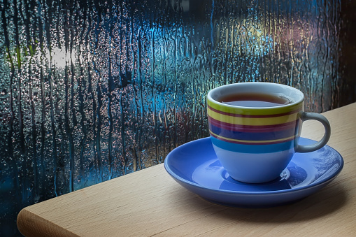 Cup of coffee against a wet blue window.