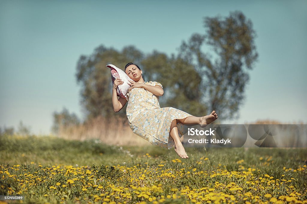 Girl with pillow soars. Girl lying on a cushion hovers over the field in weightlessness. Sleeping Stock Photo