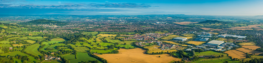 Sweeping aerial vista across a patchwork quilt of summer fields, golden crops and vibrant green pasture surrounding a country town, suburban homes and villages under blue panoramic skies. ProPhoto RGB profile for maximum color fidelity and gamut.