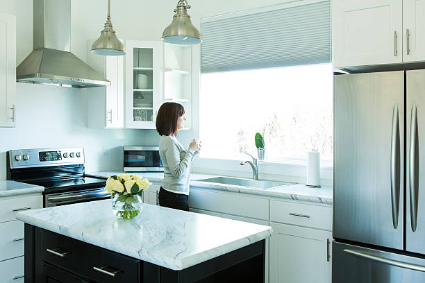 Woman Drinking Coffee in a Modern Kitchen A woman stands looking out a window in a modern kitchen. She is drinking coffee. kitchen sink photos stock pictures, royalty-free photos & images