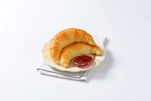 two croissants with strawberry jam on white plate and place mat