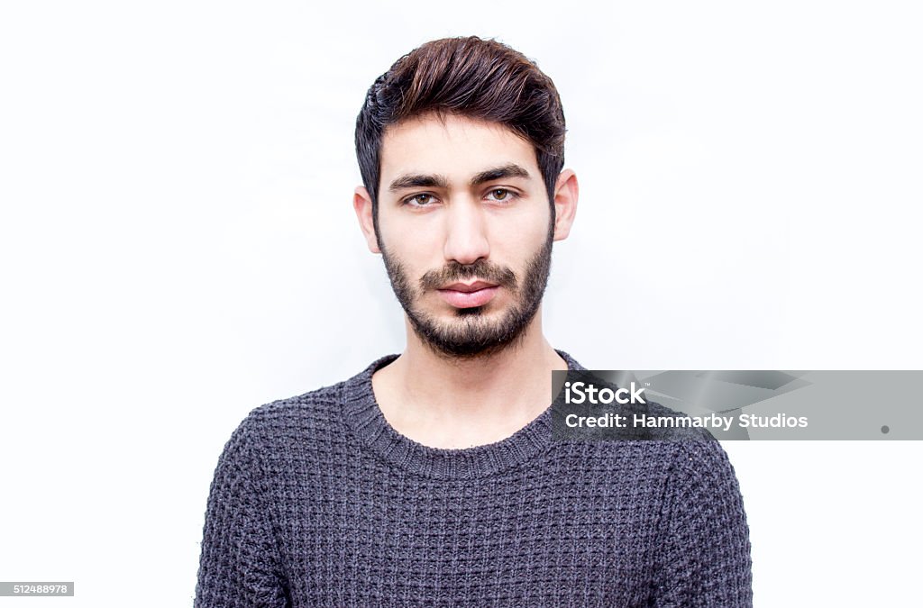 Portrait of young man over isolated on white Portrait of young man over isolated on white. Young man standing over white background and looking at camera with blank facial expression. Horizontal composition. Young man wearing a gray sweater. Front view, studio shot, developed from RAW format. Young man looking at camera with serious facial expression has got short brown hair and short beard. Young man's ethnicity belongs to Turkish ethnicity, middle eastern ethnicity. Focus on man. Portrait Stock Photo