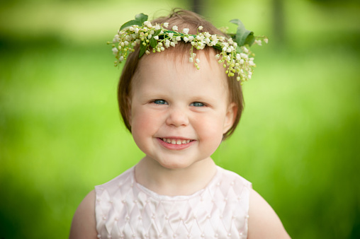 Sweet baby girl in wreath of flowers smiling outdoors