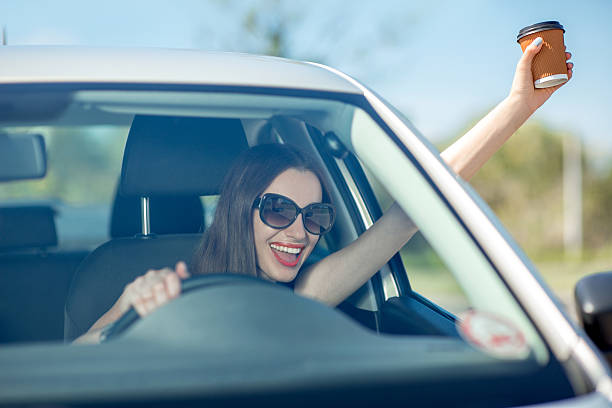 istock Young woman drinking coffee while driving her car 512492919