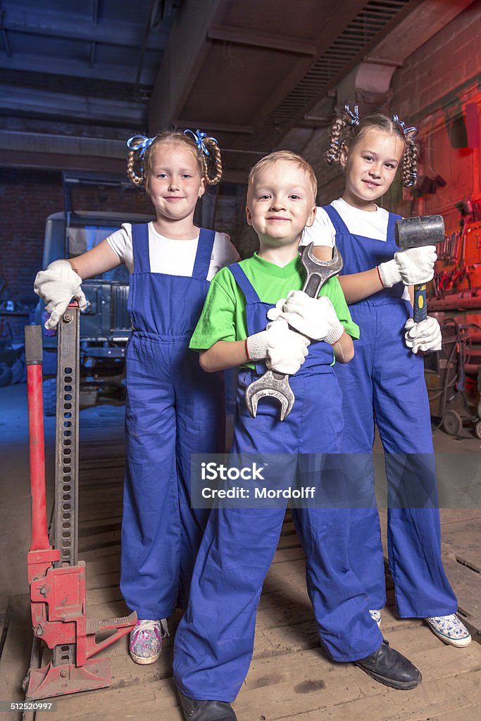 Three car mechanic Group of cheerful kids in blue overalls standing with working tools in repair shop Auto Repair Shop Stock Photo