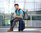 Man sitting on suitcase and sending text message