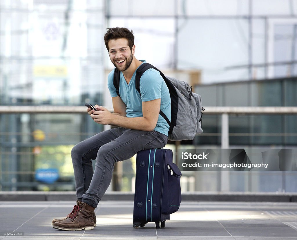 Man sitting on suitcase and sending text message Portrait of a young man sitting on suitcase and sending text message Men Stock Photo