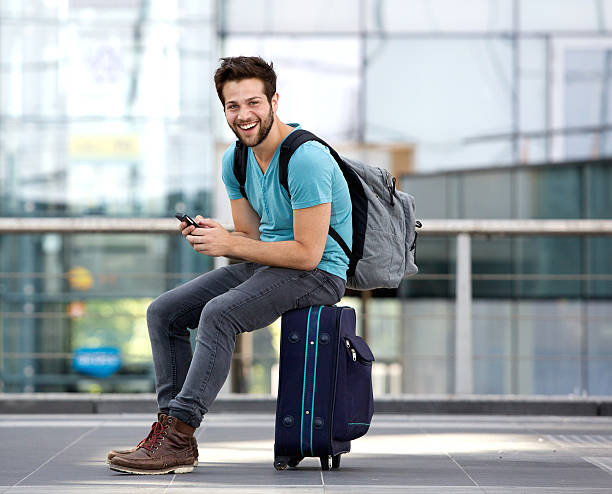homem sentado na mala e envio de mensagem de texto - tourist backpack smiling cheerful - fotografias e filmes do acervo