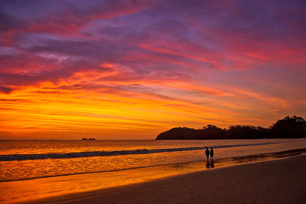 A couple wander along the sea shore at sunset one warm night in Costa Rica