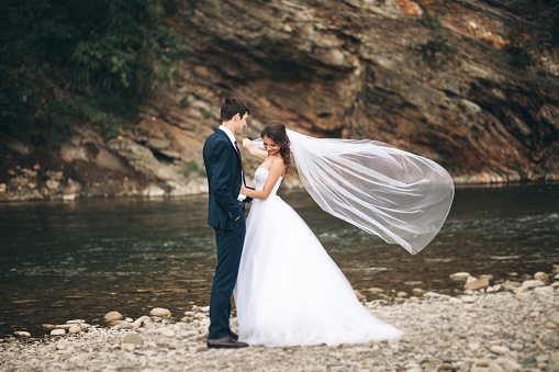 Beautifull wedding couple kissing and embracing near the shore of a mountain river with stones.