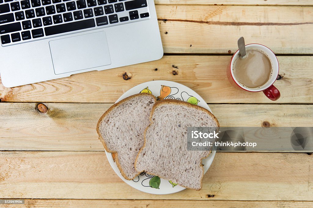 laptop, bread, and a red cup of coffee on wooden laptop, bread, and a red cup of coffee on a rustic wooden cafe table. Baked Pastry Item Stock Photo