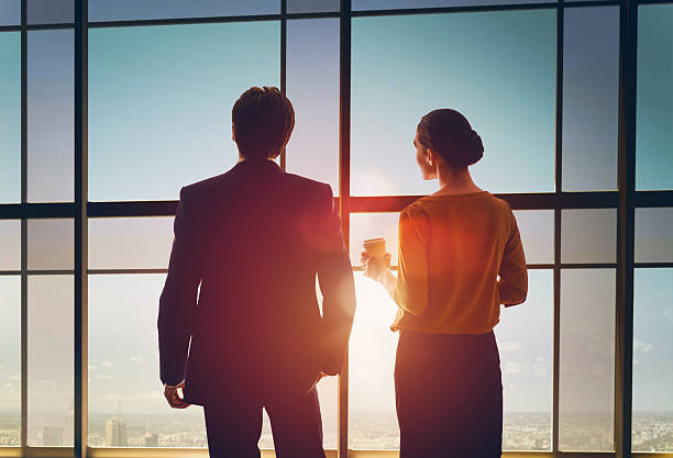 man and woman look at the city team of successful business people. two businessmen resting and talking in the office. man and woman look at the city from the window of the business center. office window night stock pictures, royalty-free photos & images
