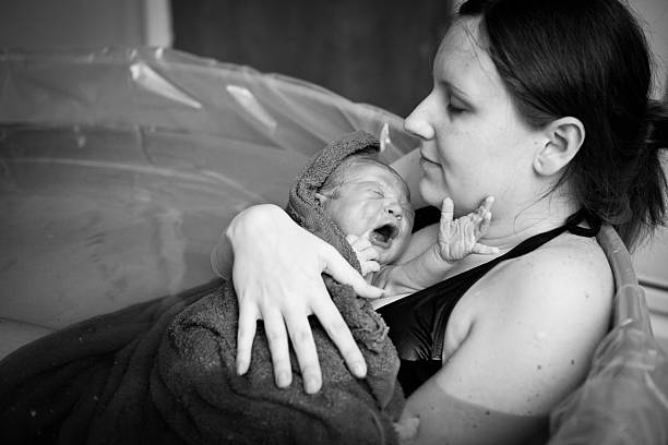 Mother Embracing Her Newborn after Home Water Birth Black and white image of a young mother holding her newborn son after giving birth at home. water birth stock pictures, royalty-free photos & images