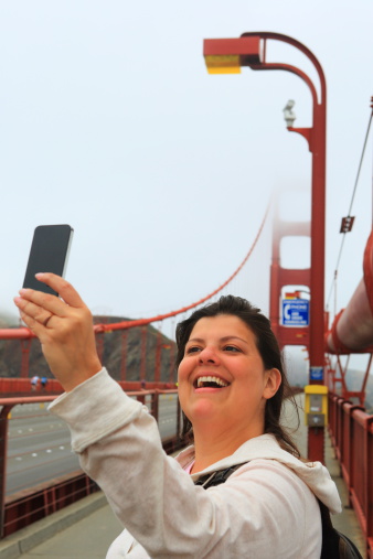 Female tourist is taking a selfie while passing by the walkway of the Golden Gate Bridge