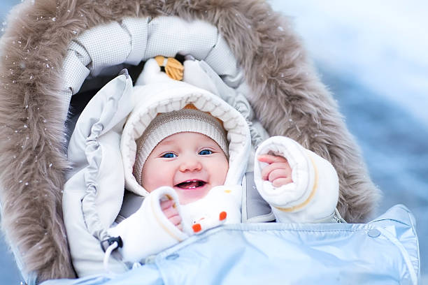 Baby in stroller in a winter park Happy laughing baby girl enjoying a walk in a snowy winter park sitting in a warm stroller with sheepskin hood wearing a white jacket and hat baby stroller winter stock pictures, royalty-free photos & images