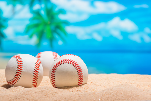 Three baseballs sitting on the beach for the Grapefruit League in Florida for Spring Training, with palm trees and ocean in the background