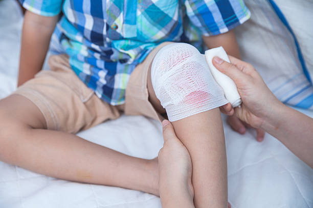 Child injured. Mother bandaging son's knee. stock photo