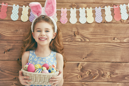 Cute little child girl wearing bunny ears on Easter day. Girl holding basket with painted eggs.