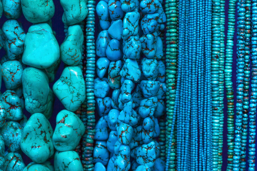 A close-up, full-frame of turquoise strands of beads and necklaces hanging in a shop.