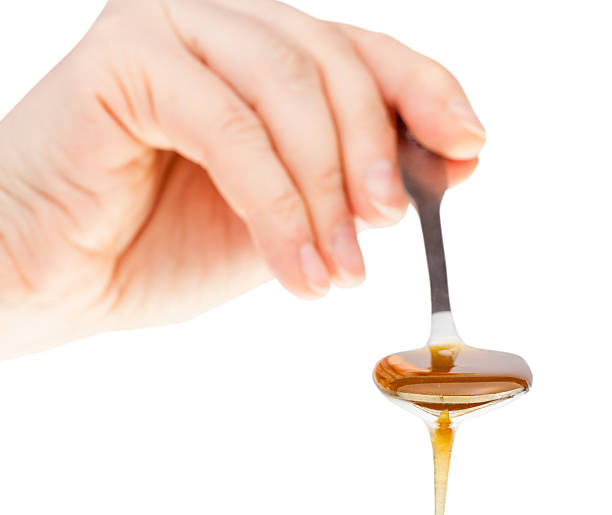 istock hand holds metal spoon with clear honey 512573198