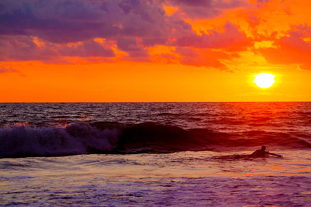 Surfers waiting for wave at sunset in Costa Rica A surfer waits for a wave at sunset in the tropical waters of Costa Rica.  rr costa rican sunset stock pictures, royalty-free photos & images