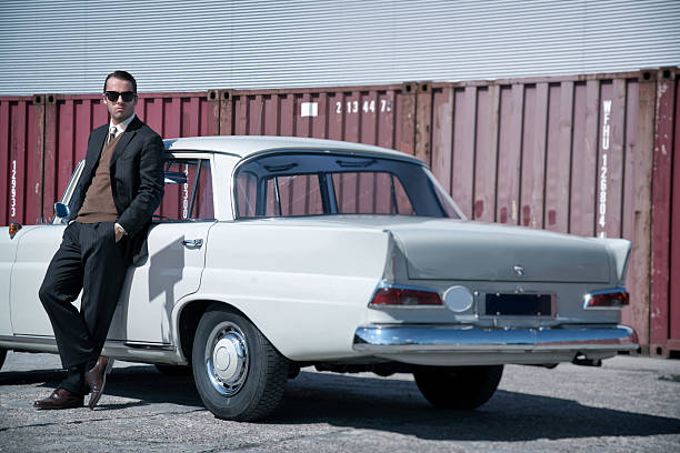 Retro 60s fashion business man wearing grey suit and sunglasses. Retro 60s fashion business man wearing grey suit and black sunglasses standing against classic car. organized crime photos stock pictures, royalty-free photos & images