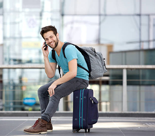 istock Young man sitting on suitcase and calling by cellphone 512577551