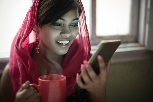 Beautiful woman near window with coffee mug using smartphone.