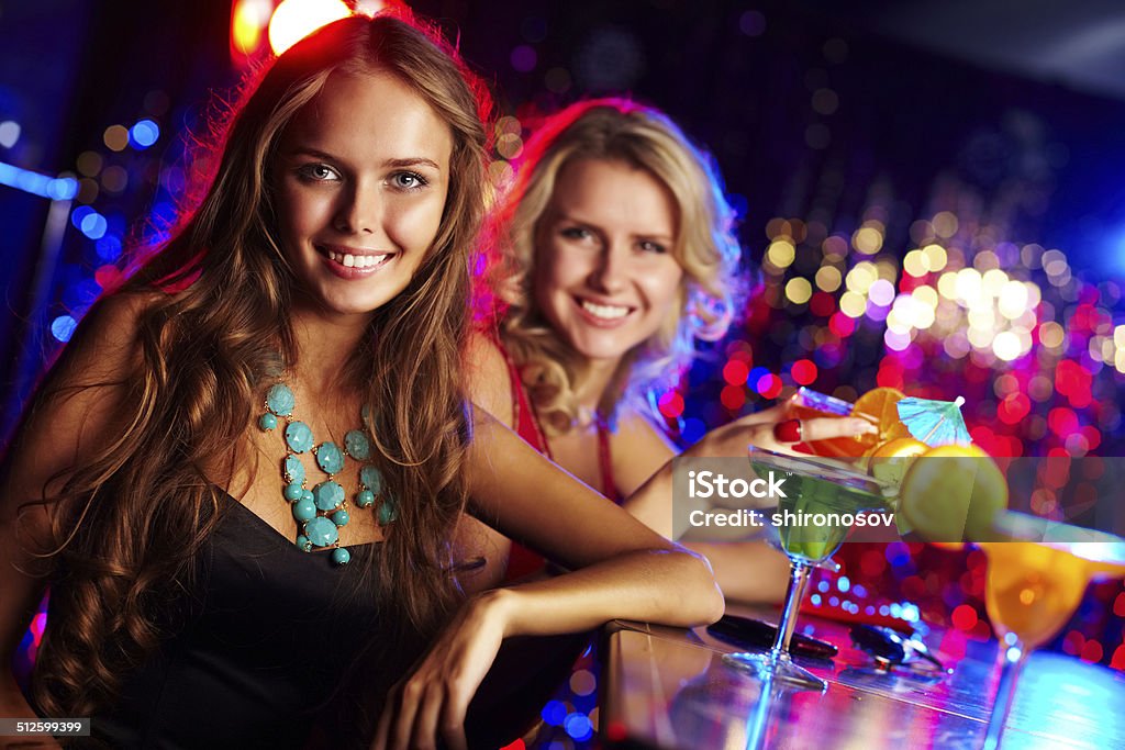 Girl in bar Image of happy girl looking at camera with her friend behind Adult Stock Photo