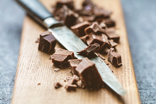 cutting milk chocolate and dark chocolate into pieces with a knife on a wooden cutting board.
