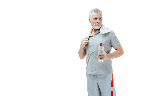 Horizontal photo of silver haired senior sportsman isolated on white background. Man with towel on neck holding bottle of water