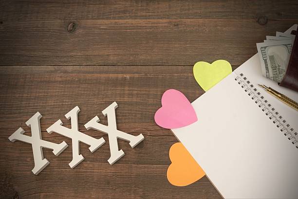 XXX Love Sign, Opened Notepad And Male Wallet With Cash White XXX Love Sign On Wood Background, Opened Notepad With Blank Page And Three Color Heart Sticker, Golden Pen And Male Wallet With Dollar Cash menage trois stock pictures, royalty-free photos & images