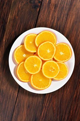 Orange fruit slices on white plate over wooden background, top view