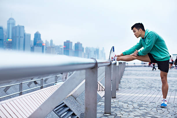 Running through the urban jungle Shot of a young asian man warming up for a jog along the Hong Kong skyline warm up exercise stock pictures, royalty-free photos & images