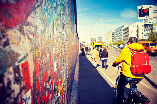 East Side Gallery Berlin, Germany - April 17, 2014: A tourist on a bike rides along the East Side Gallery, an international memorial for freedom with paintings by artists from all over the world on one of the longest remaining sections of the Berlin Wall. friedrichshain photos stock pictures, royalty-free photos & images