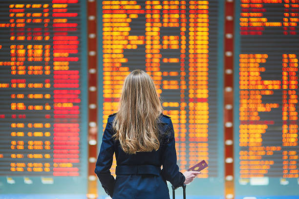 Young woman in international airport Young woman in international airport looking at the flight information board, checking her flight cancellation stock pictures, royalty-free photos & images