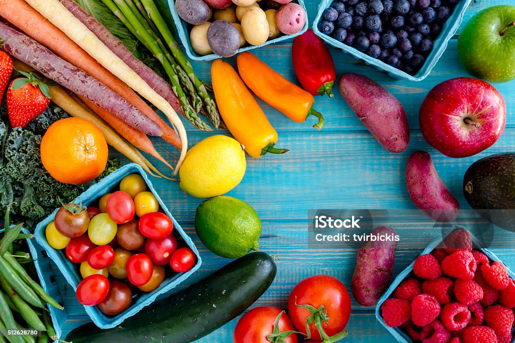 Assorted Fruits and Vegetables Background Variety of fresh raw organic fruits and vegetables in light blue containers sitting on bright blue wooden background Vegetable Stock Photo