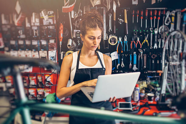 Female Bicycle Mechanic Portrait of a young female bicycle mechanic using a laptop. bicycle shop stock pictures, royalty-free photos & images