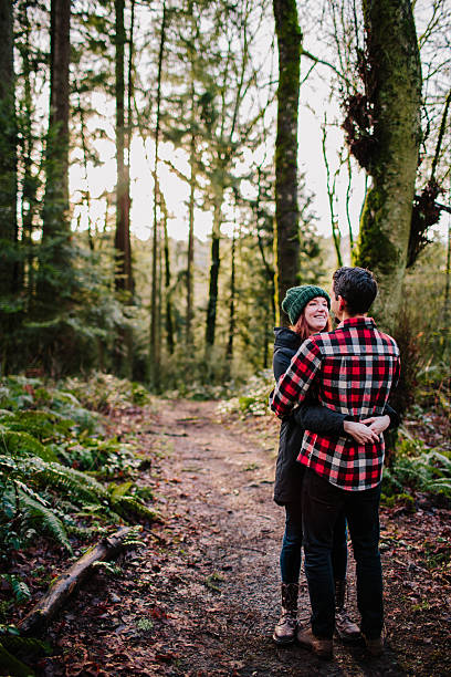 A young couple pause during their hike to enjoy a playful happy moment and a hug. They are embracing and laughing while the sun shines through the trees. Located in Forest Park, Portland, Oregon.