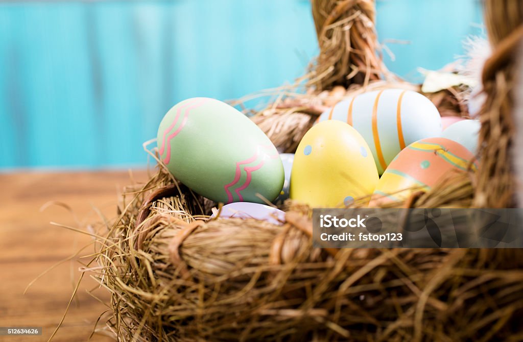 Colorful Easter eggs in straw basket.  Blue background. Happy Easter!  Close-up image of decorated, multi-colored Easter eggs lying in a straw basket on a rustic, vintage wooden table.  Blue background. Ready for an Easter Egg Hunt!   Great for Easter and spring themes.  No people. Pastel colors. Animal Egg Stock Photo