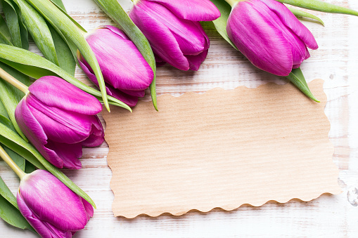 A bouquet of tulips and an empty paper card on wooden background