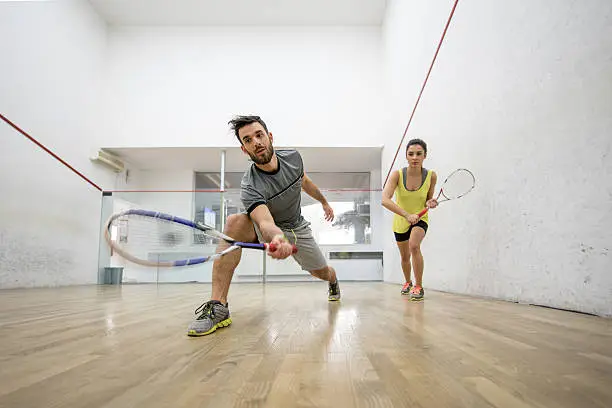 Low angle view of young couple exercising racketball on a court. Focus is on man reaching for the ball.