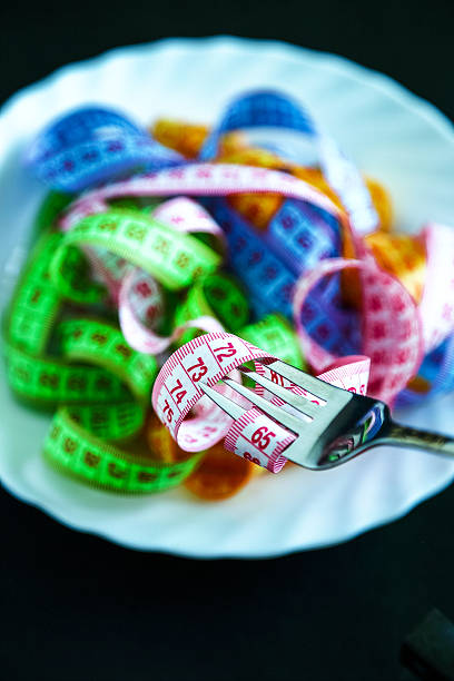 maßband auf einem teller wie ein strang von nudeln - healthy eating fork tape measure still life stock-fotos und bilder