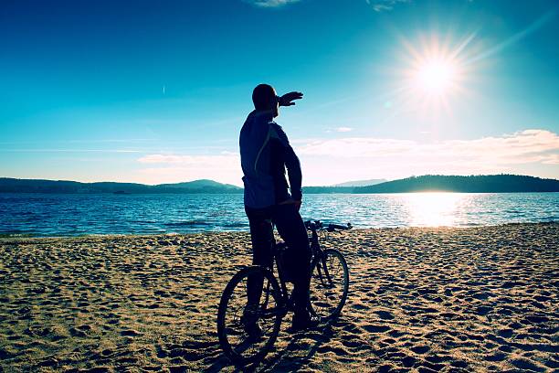 istock Young man cyclist silhouette on beach. Spring n at lake. 512688800