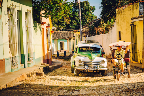 Trinidad, Cuba - March 23, 2015: Old vintage car and Cycle Rikshaw in the cobblestone street in the town of Trinidad, Cuba. 