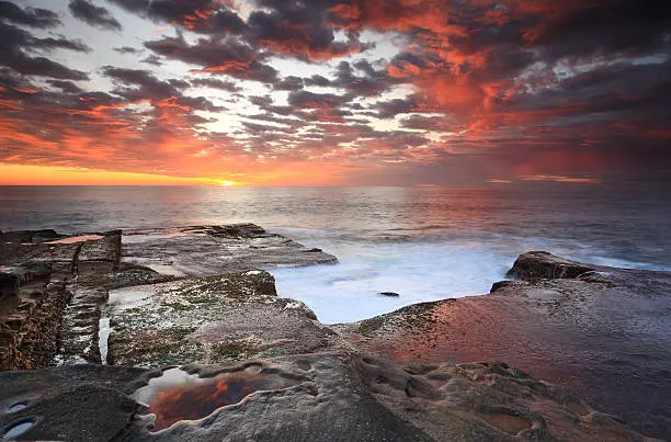 Stunning sunrise over Maroubra, rich colours in the sky and their reflections as water flows over and around rocks.  Some motion in the retreating water and mosses.
