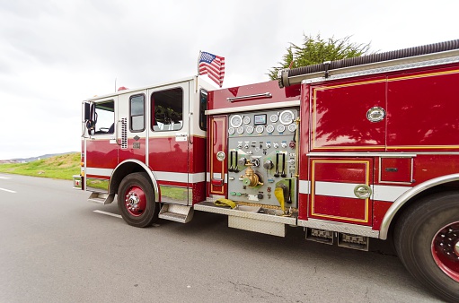 An american fire brigade truck in response, in San Francisco, California, United States of America. A view of the red vehicle on the move and the american flag waving.